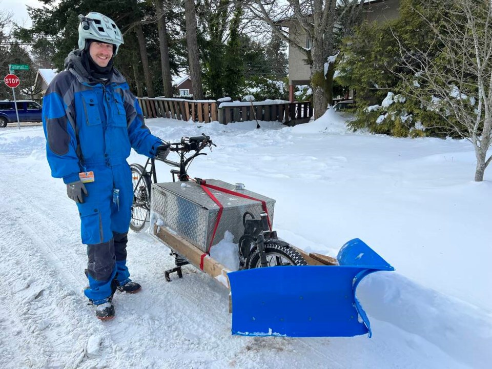 A man standing next to a cargo bike fitted with a homemade snowplow 