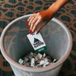 A feminine looking hand with red nails drops a Web Summit badge into a trash can.